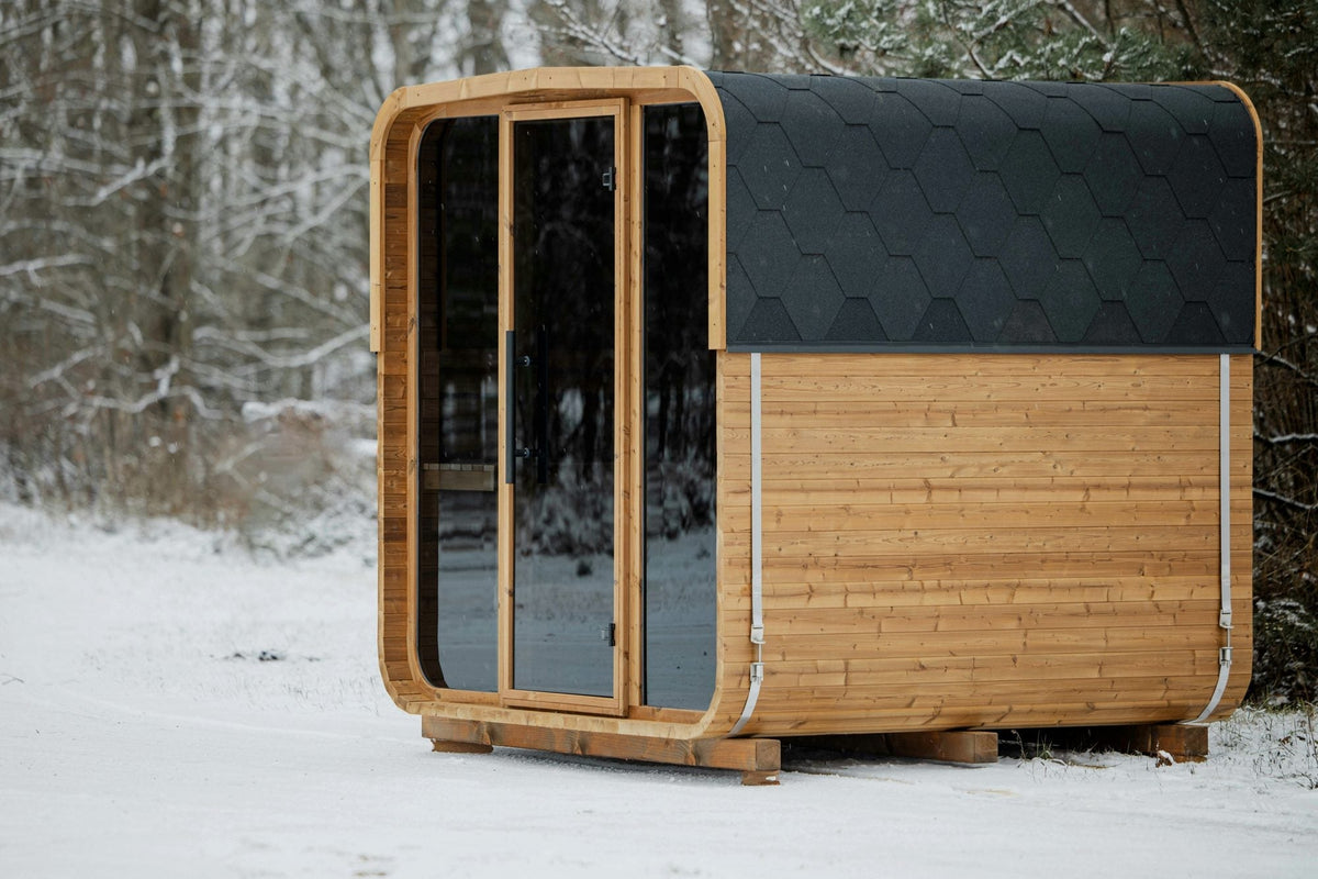Wooden cube sauna with a glass front standing in a snowy forest