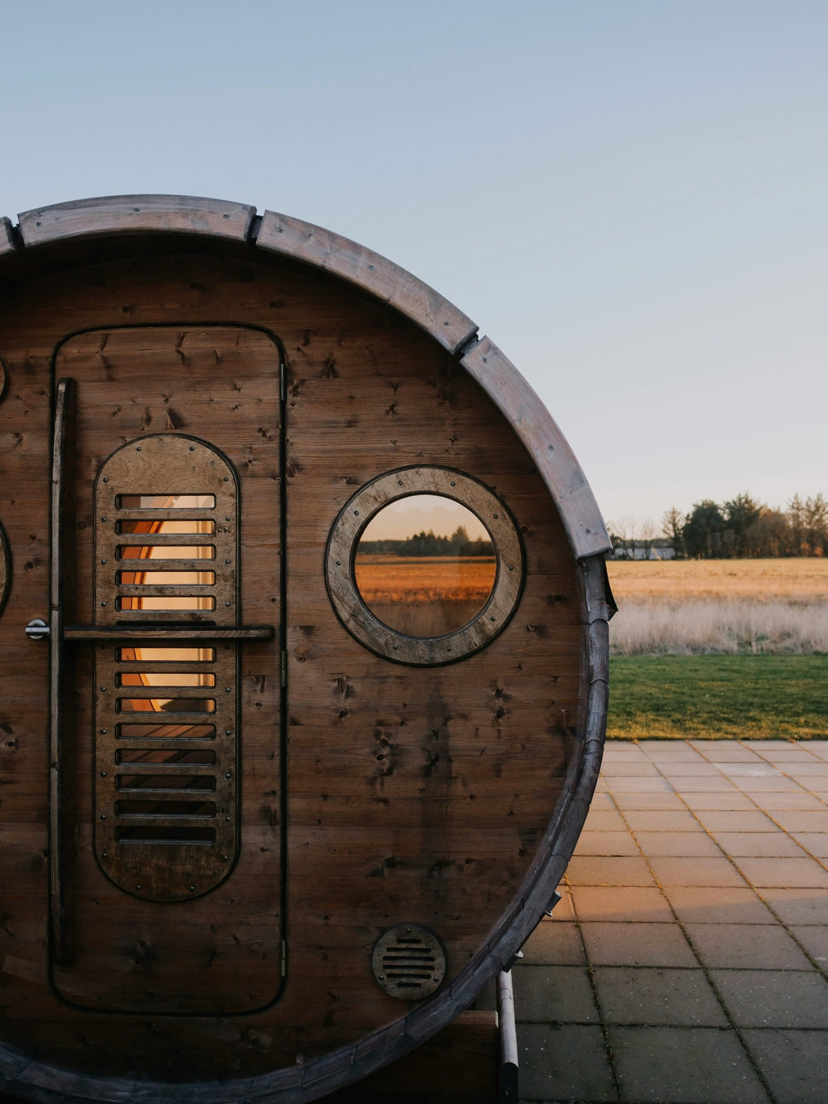 Round barrel sauna exterior with porthole window in an open field